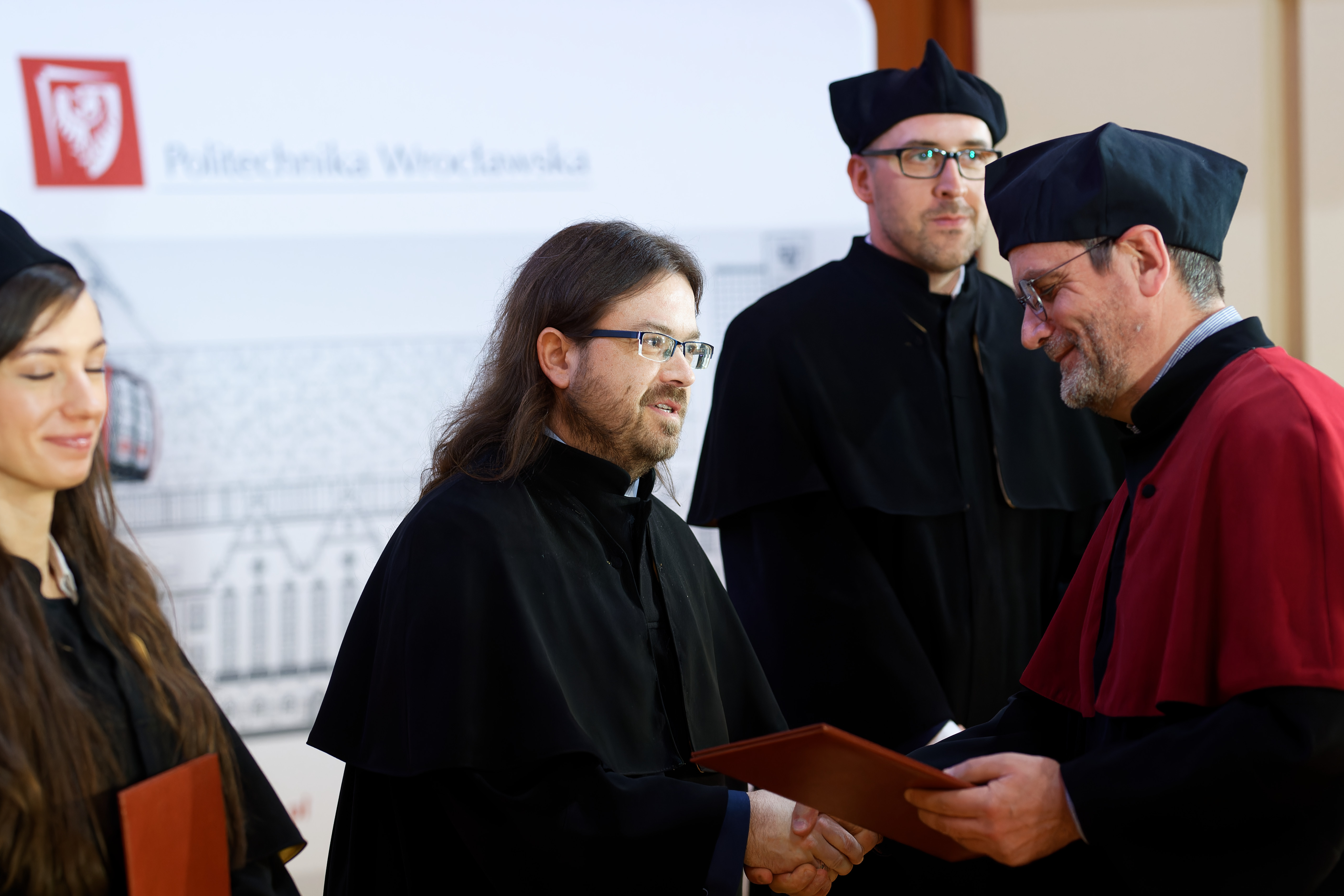 Prorektor do spraw nauki wręcza Mariuszowi Uchrońskiemu dyplom podczas uroczystości w auli.